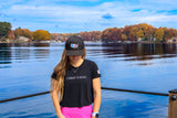 Person wearing a black t-shirt with 'CHRIST IS KING' and a cap, standing by a lake with autumn trees.